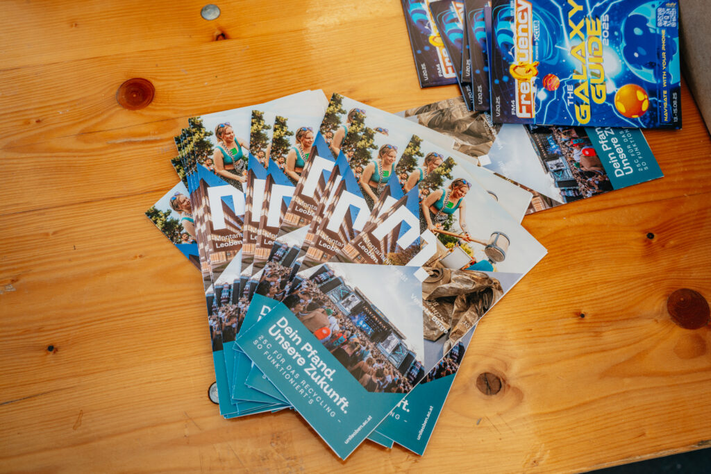Mehrere bunte Festivalflyer der Montanuniversität Leoben liegen auf einem Holztisch